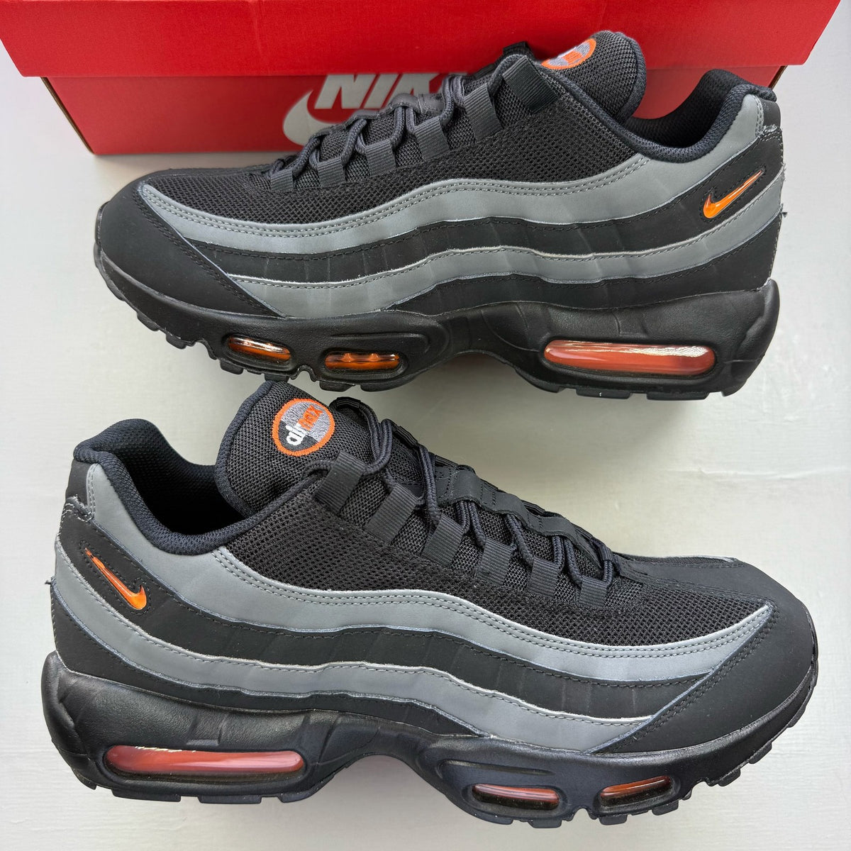 Nike Air Max 95 black grey trainers with safety orange accents and logo detailing.