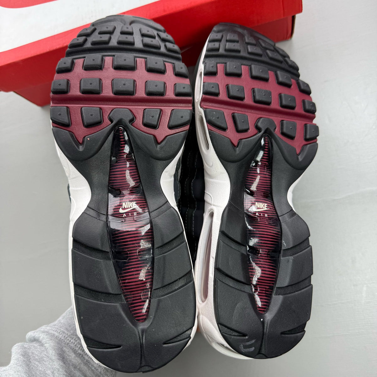 Nike black trainers with red accents and grey detailing, featuring iconic Air Max design.