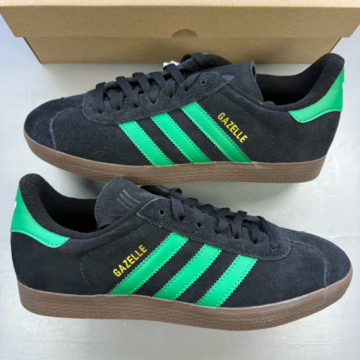Adidas black Gazelle trainers with green accents and classic logo detailing.