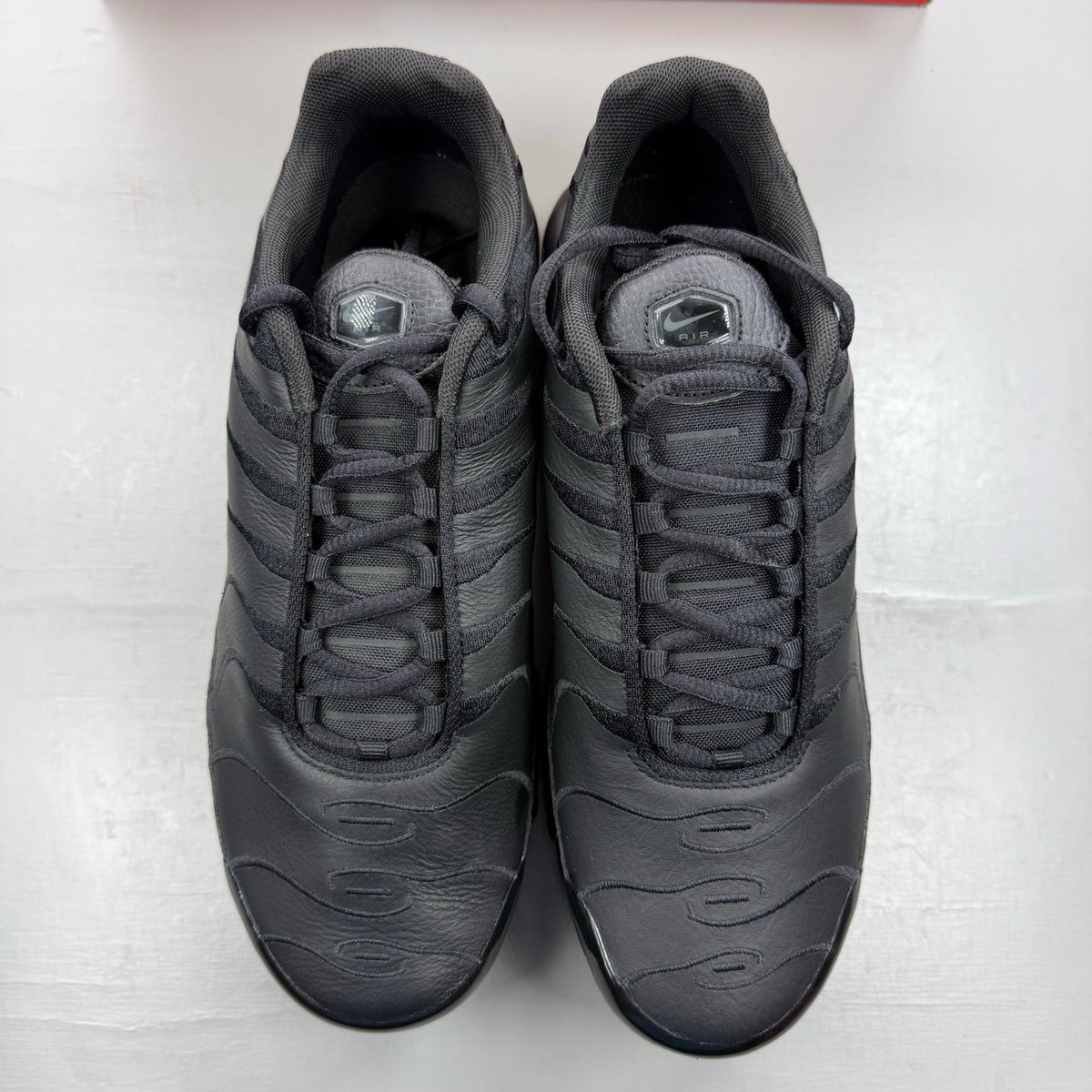 Nike Air Max Plus TN black leather trainers with distinctive wave pattern and logo.