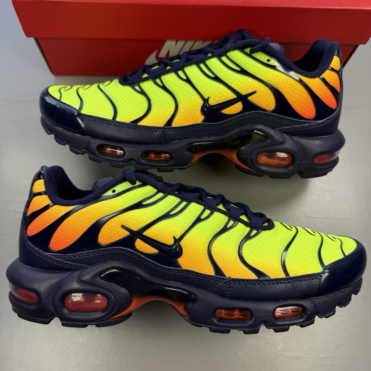 Nike Air Max Plus TN yellow trainers with orange accents and signature swoosh logo.