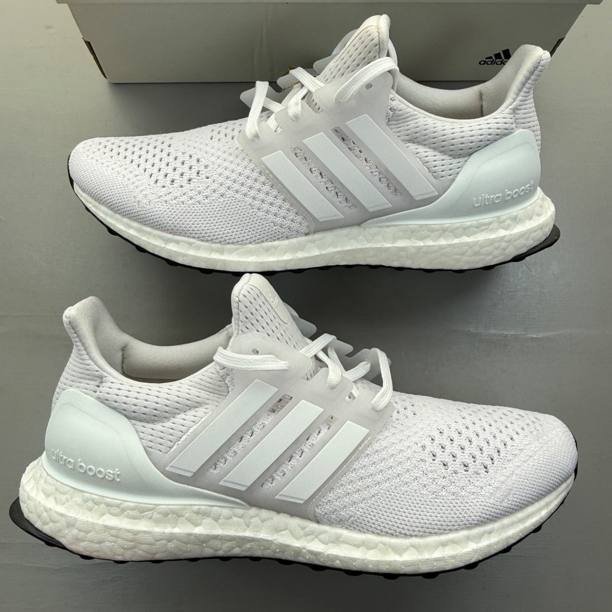 Adidas Ultra Boost 1.0 white running trainers with textured knit upper and signature three stripes.