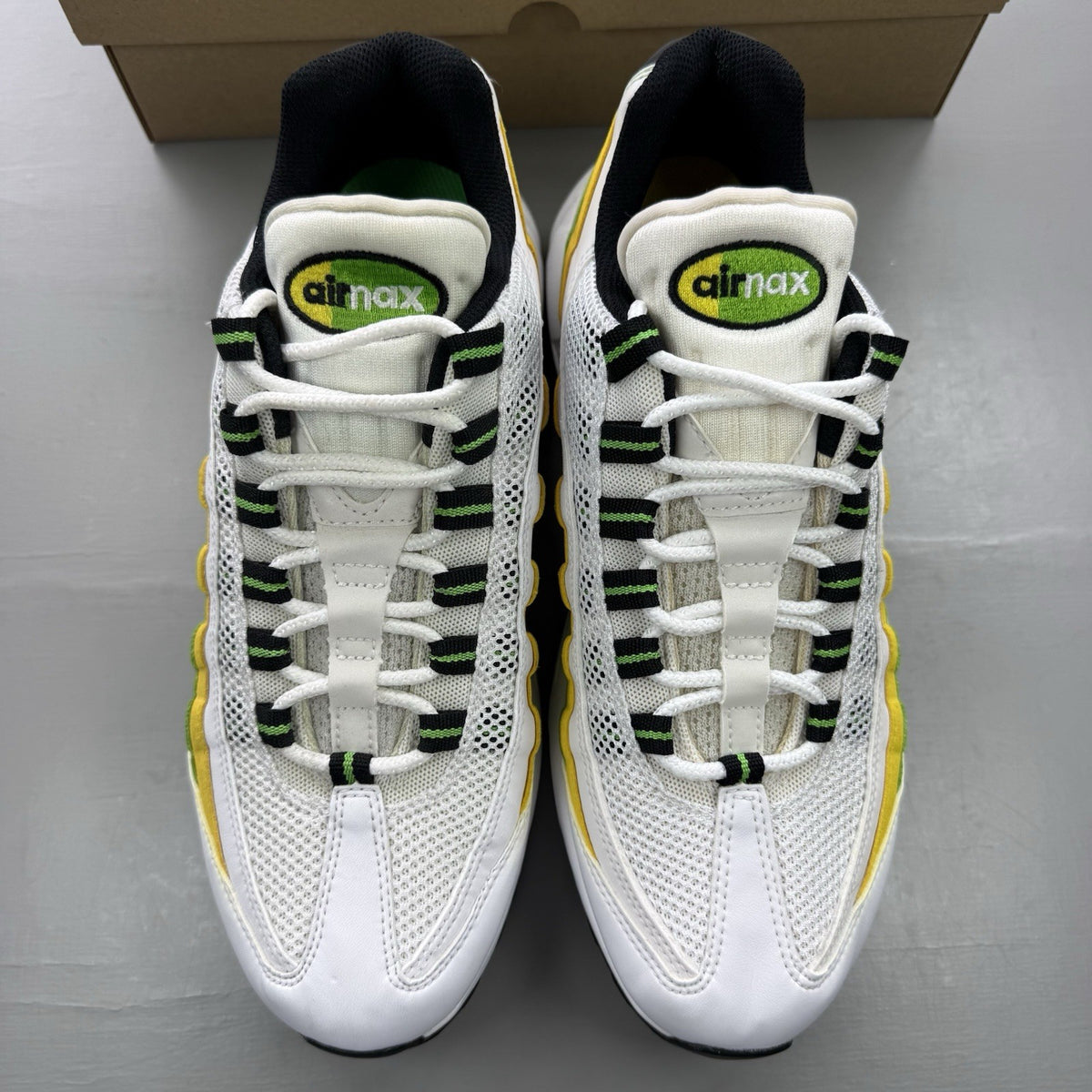 Nike Air Max 95 white trainers with green and yellow accents, featuring iconic logo details.