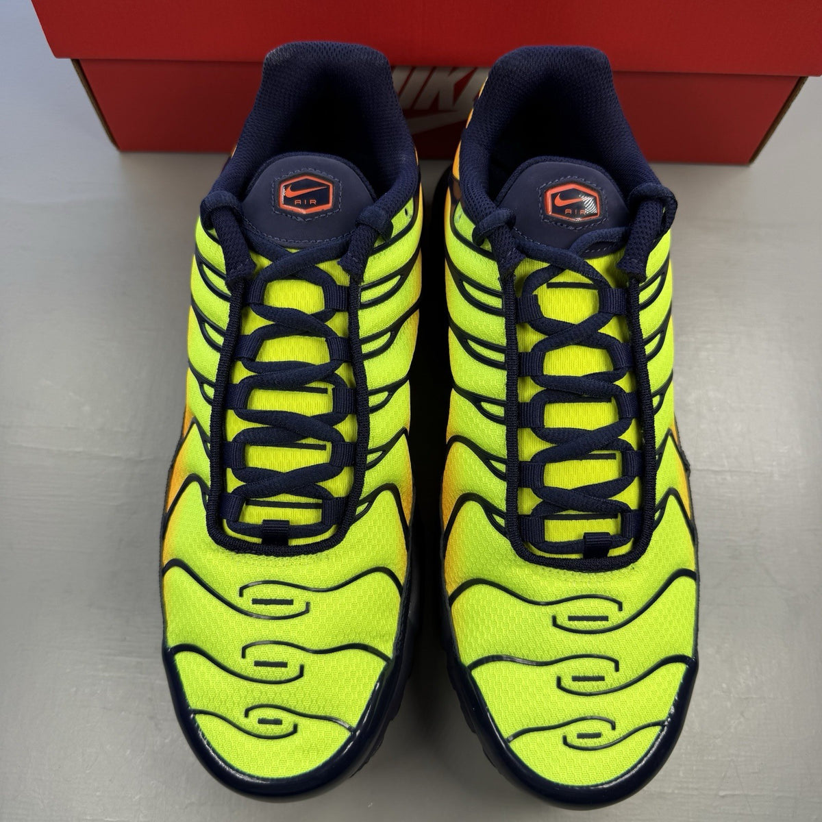 Nike Air Max Plus TN yellow trainers with orange accents and signature swoosh logo.