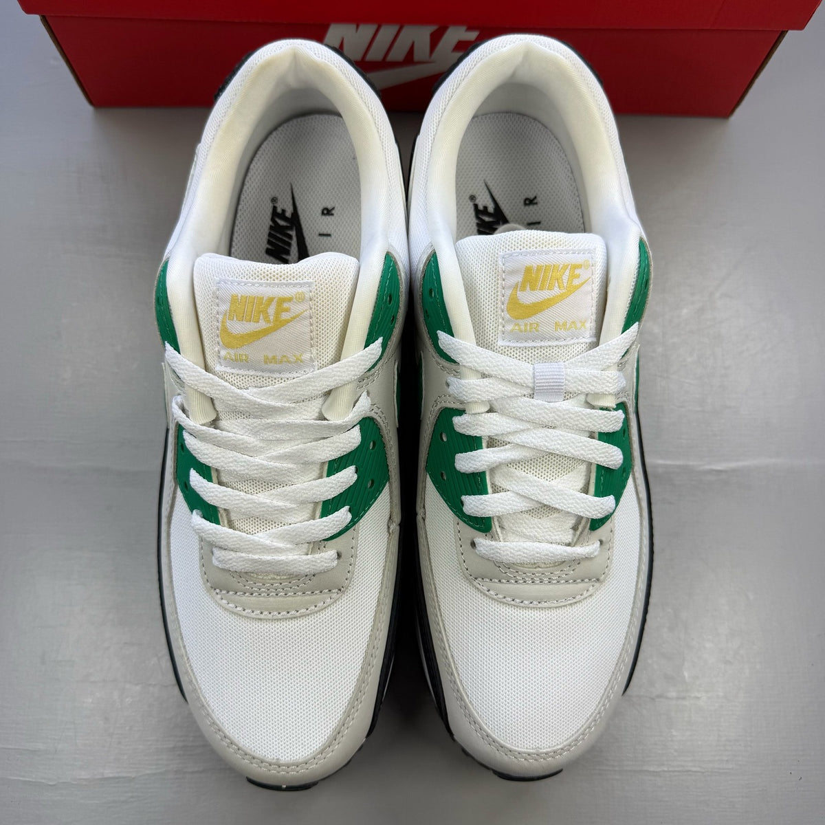Nike Air Max 90 white trainers with green and black accents, featuring iconic logo details.