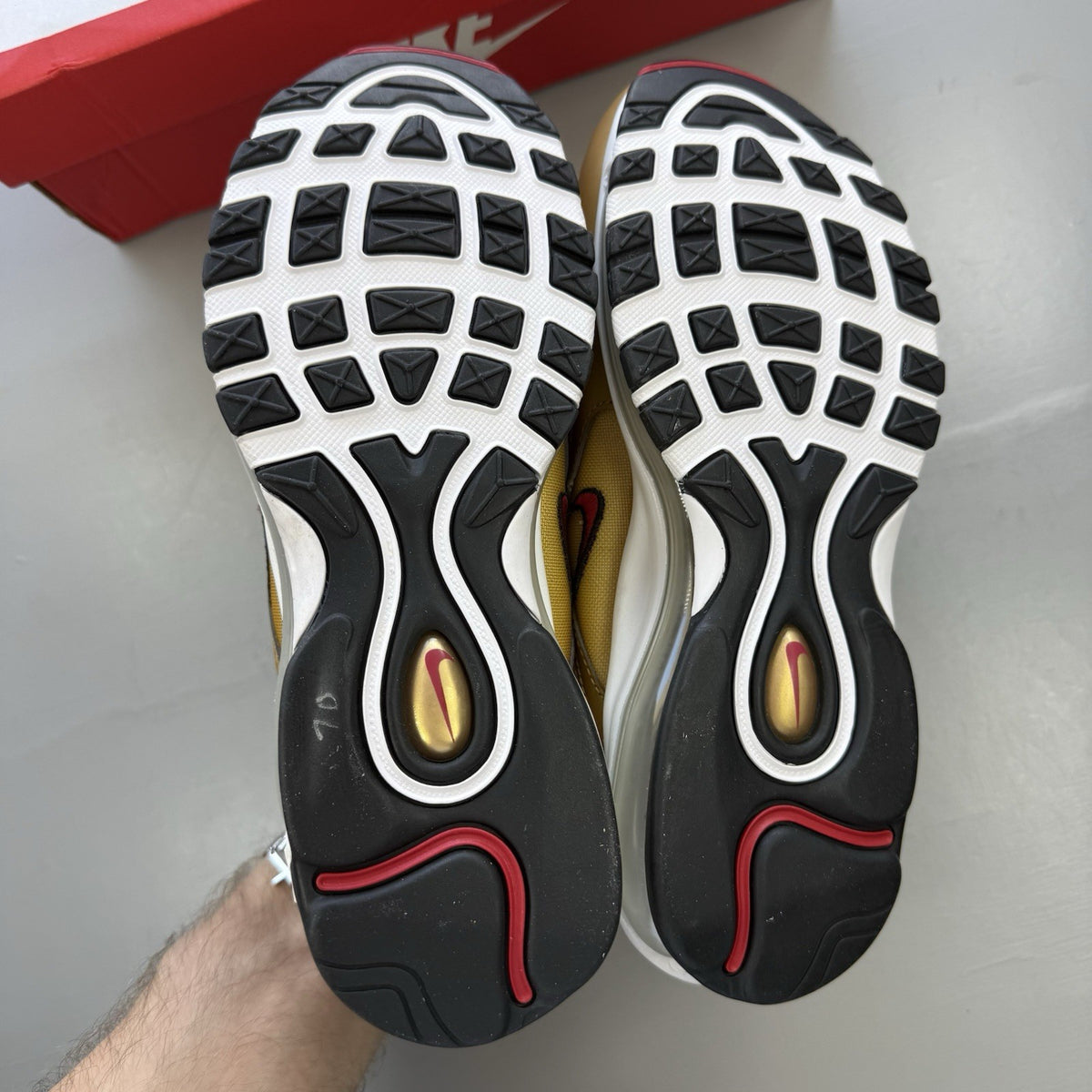 Nike Air Max 97 gold trainers with white and black accents, featuring a sleek design.