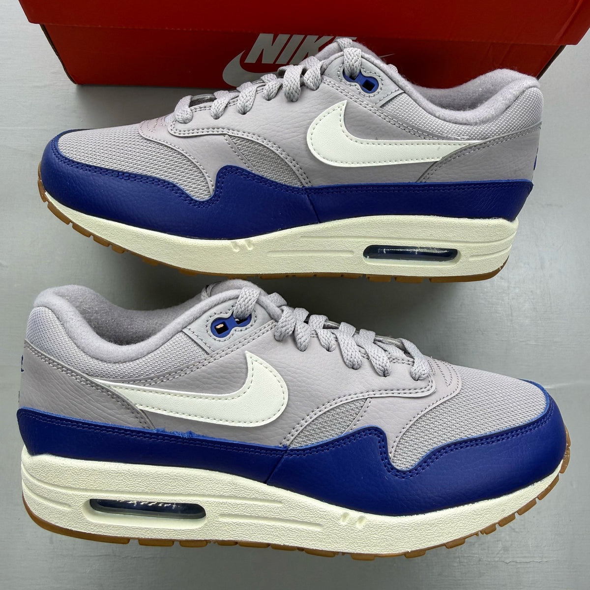 Nike Air Max 1 grey trainers with royal blue accents and signature logo.