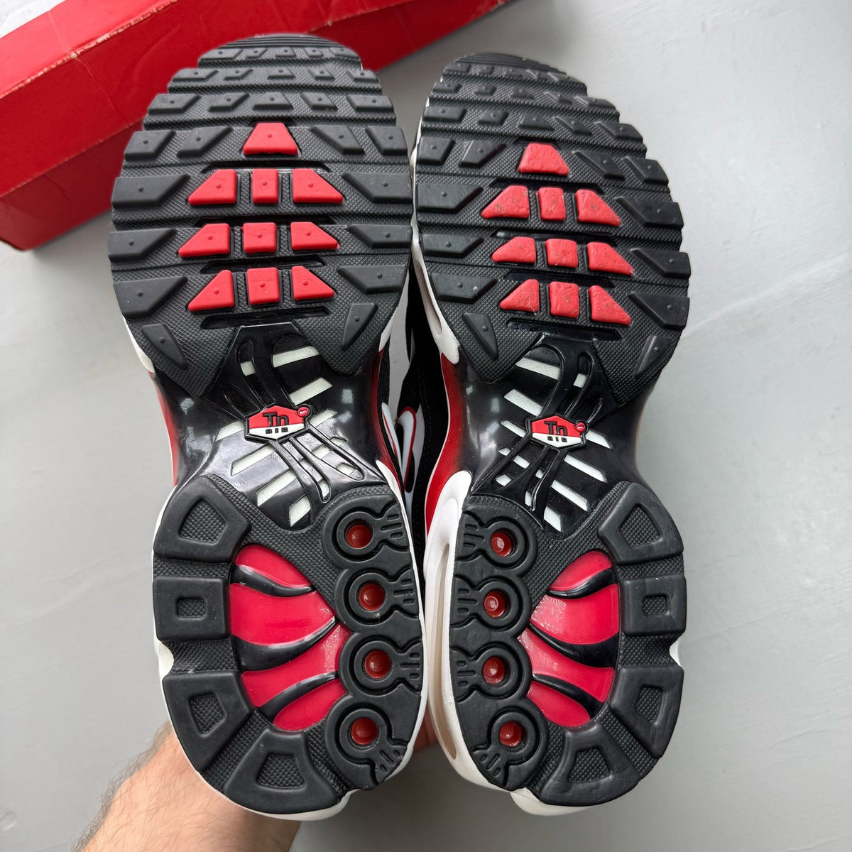 Nike Air Max Plus TN black trainers with white and university red accents, mesh material.