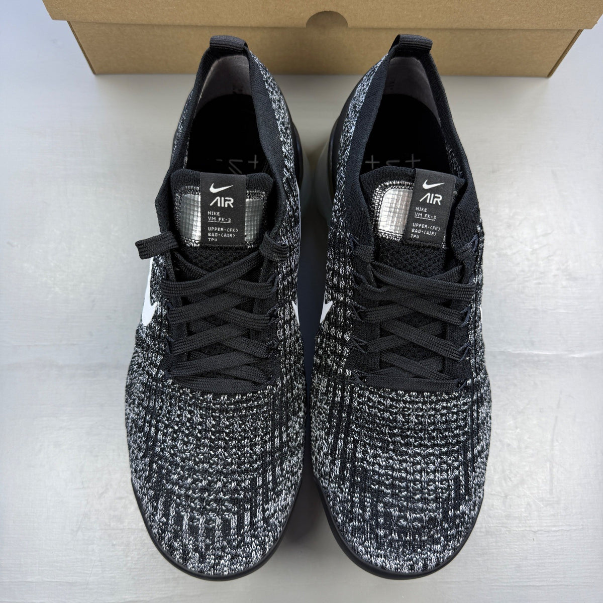 Nike athletic shoes black Flyknit design with white accents and VaporMax sole.