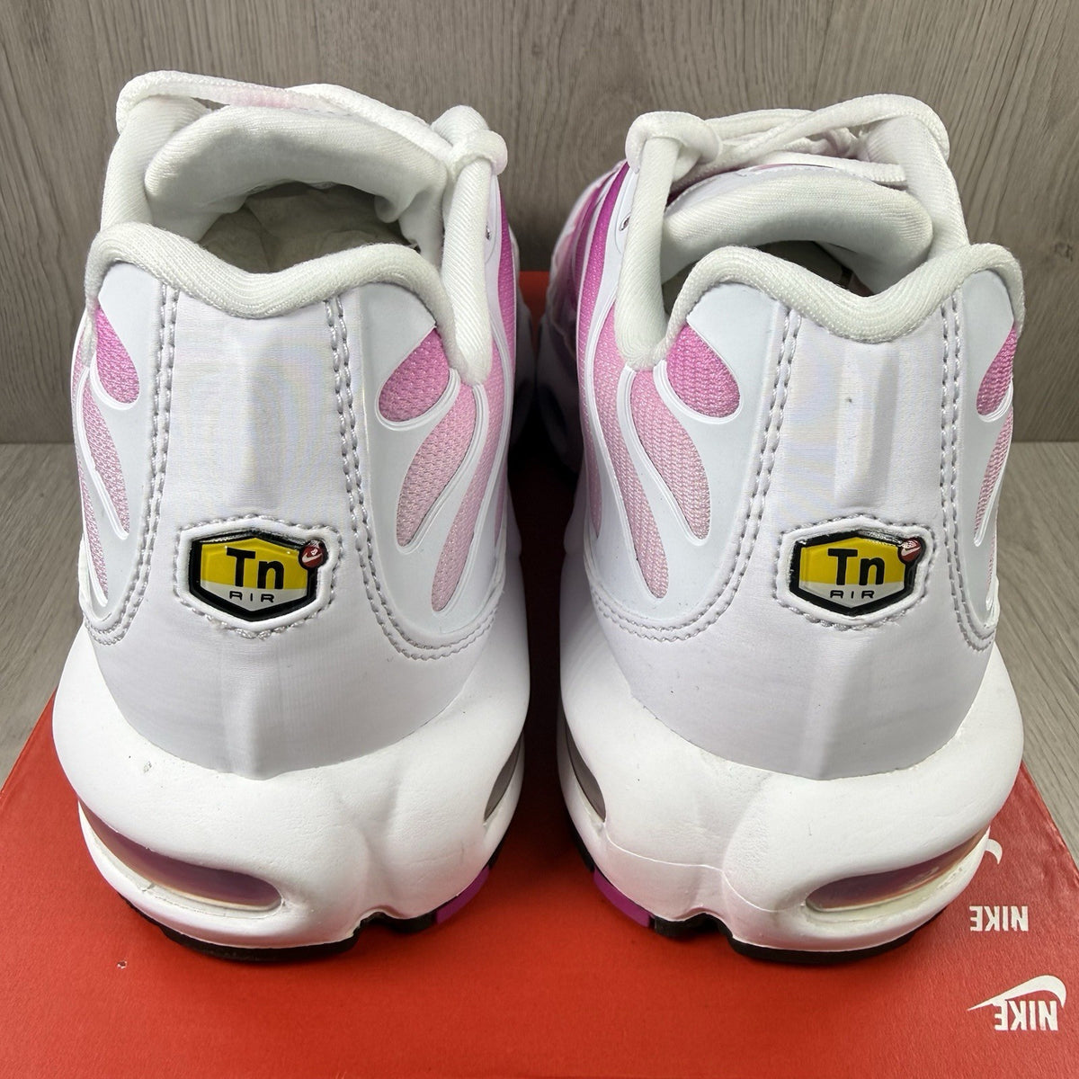 Nike Air Max Plus TN white trainers with fire pink foam fade and logo detailing.