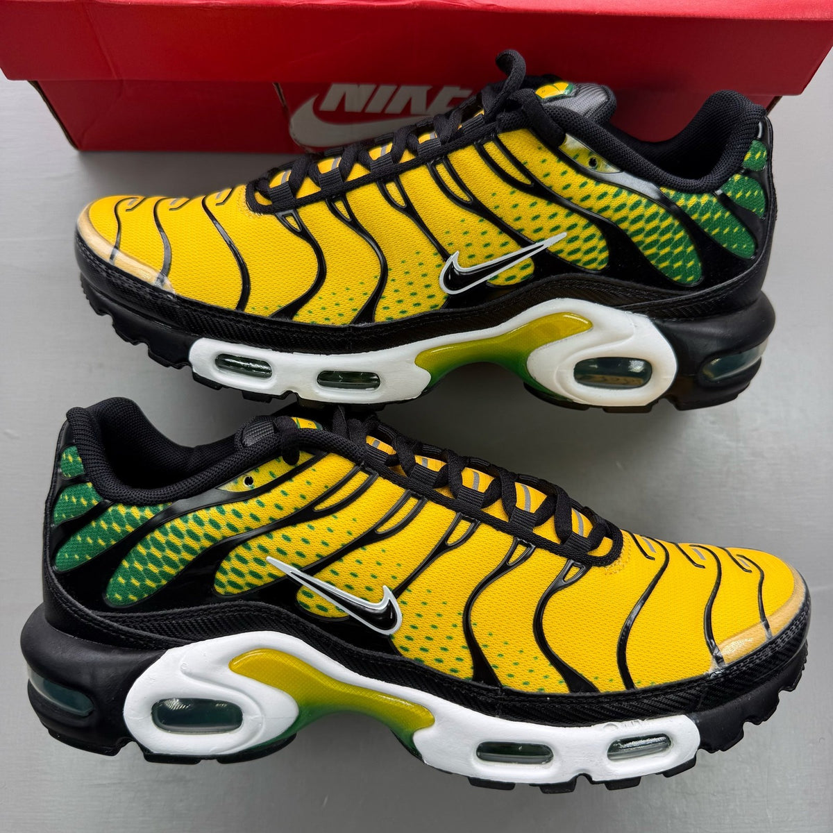 Nike black trainers featuring Air Max Plus design and vibrant yellow accents.