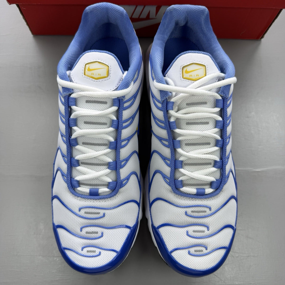 Nike Air Max Plus TN white trainers with blue and yellow accents, featuring logo detailing.