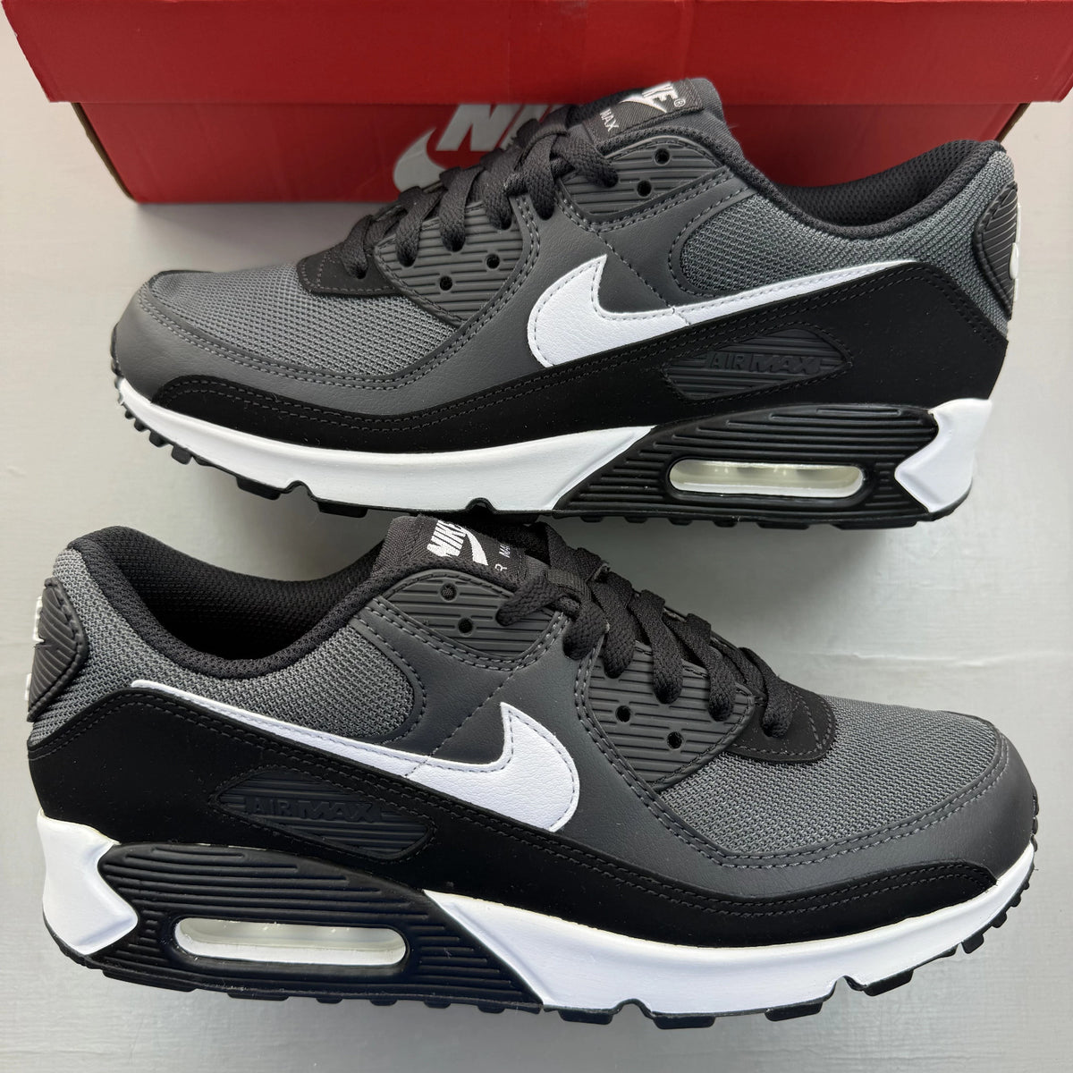 Nike Air Max 90 grey trainers with black and white accents, featuring logo details.