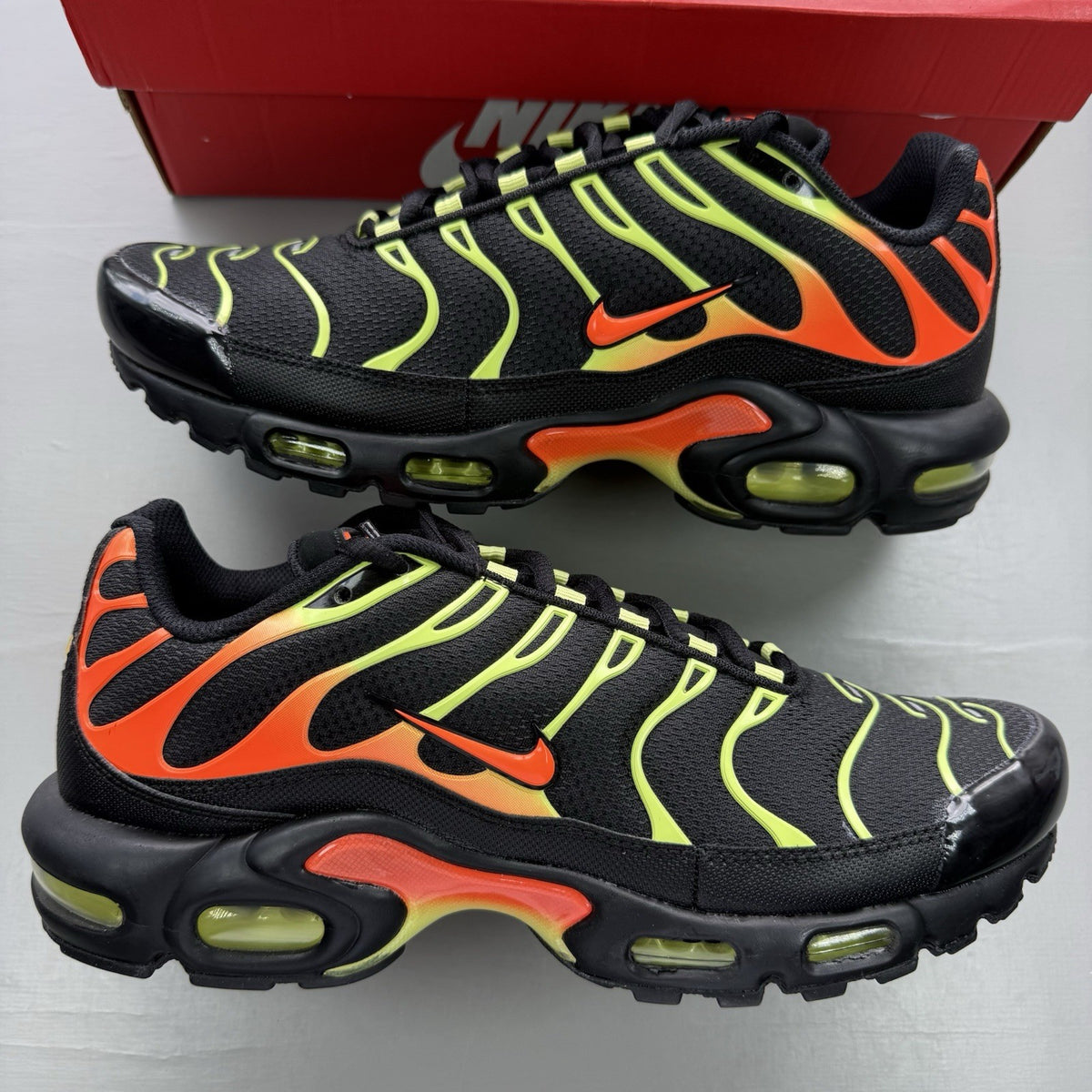 Nike Air Max Plus TN black trainers with vibrant orange and volt accents, mesh material.
