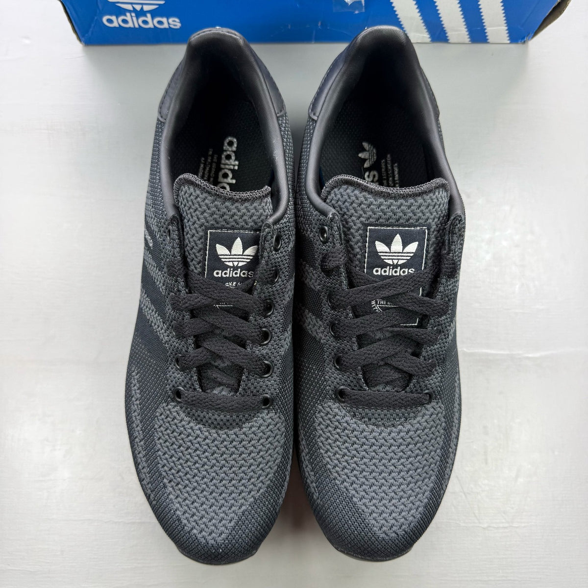 Adidas black grey LA Trainer sneakers with woven upper and iconic three-stripe logo.
