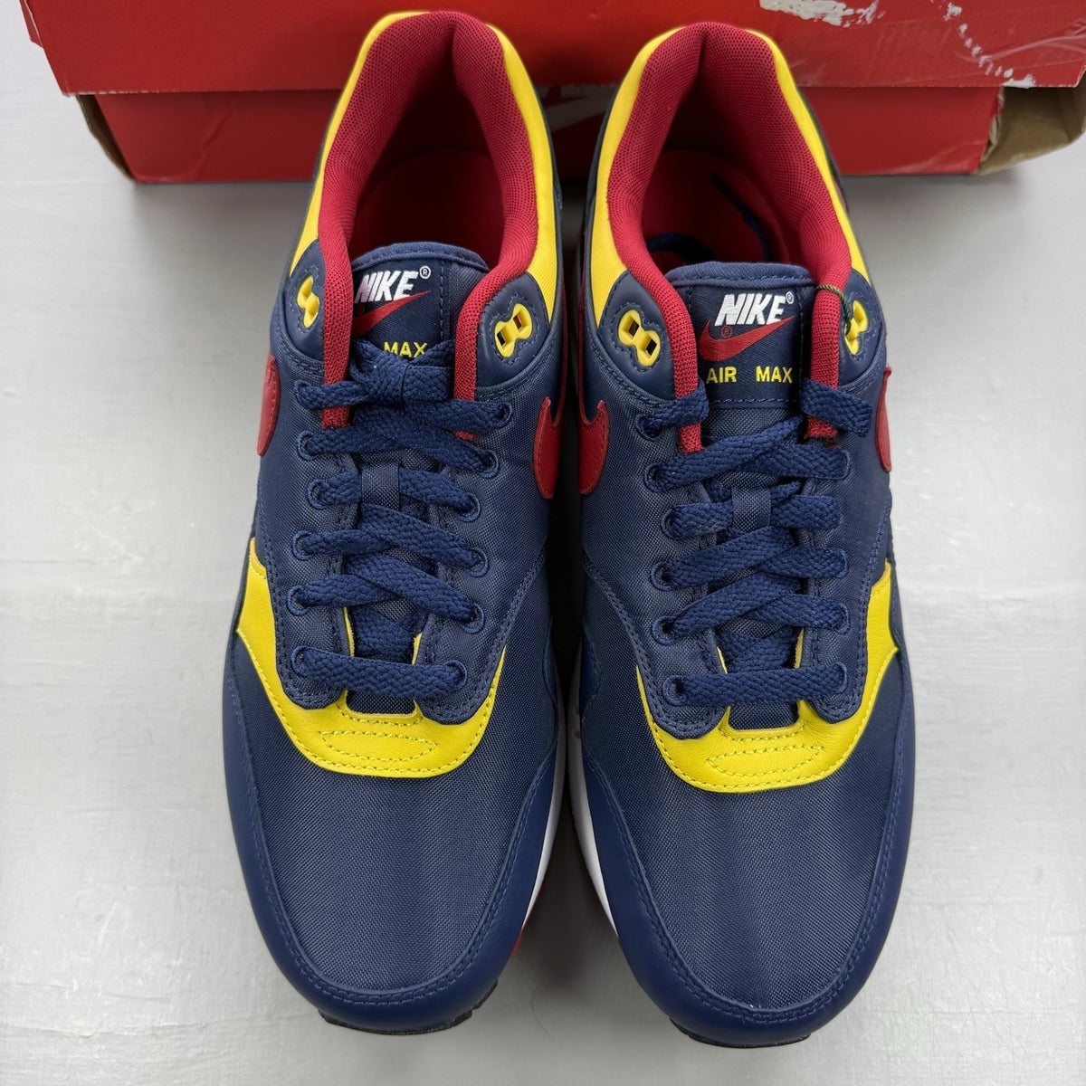 Nike Air Max 1 trainers blue with red and yellow accents, featuring iconic logo and design.
