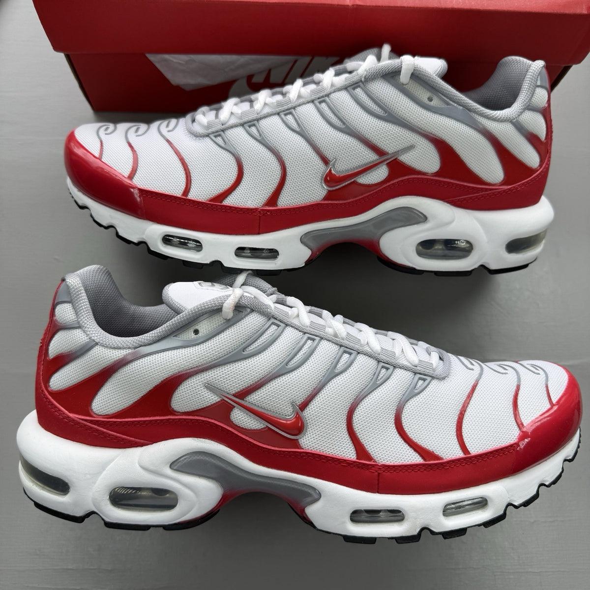 Nike Air Max Plus TN white trainers with university red and grey accents, featuring signature logo.