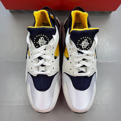 Nike Air Huarache white sneakers with yellow maize and navy accents, featuring logo details.