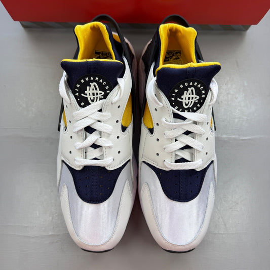 Nike Air Huarache white sneakers with yellow maize and navy accents, featuring logo details.