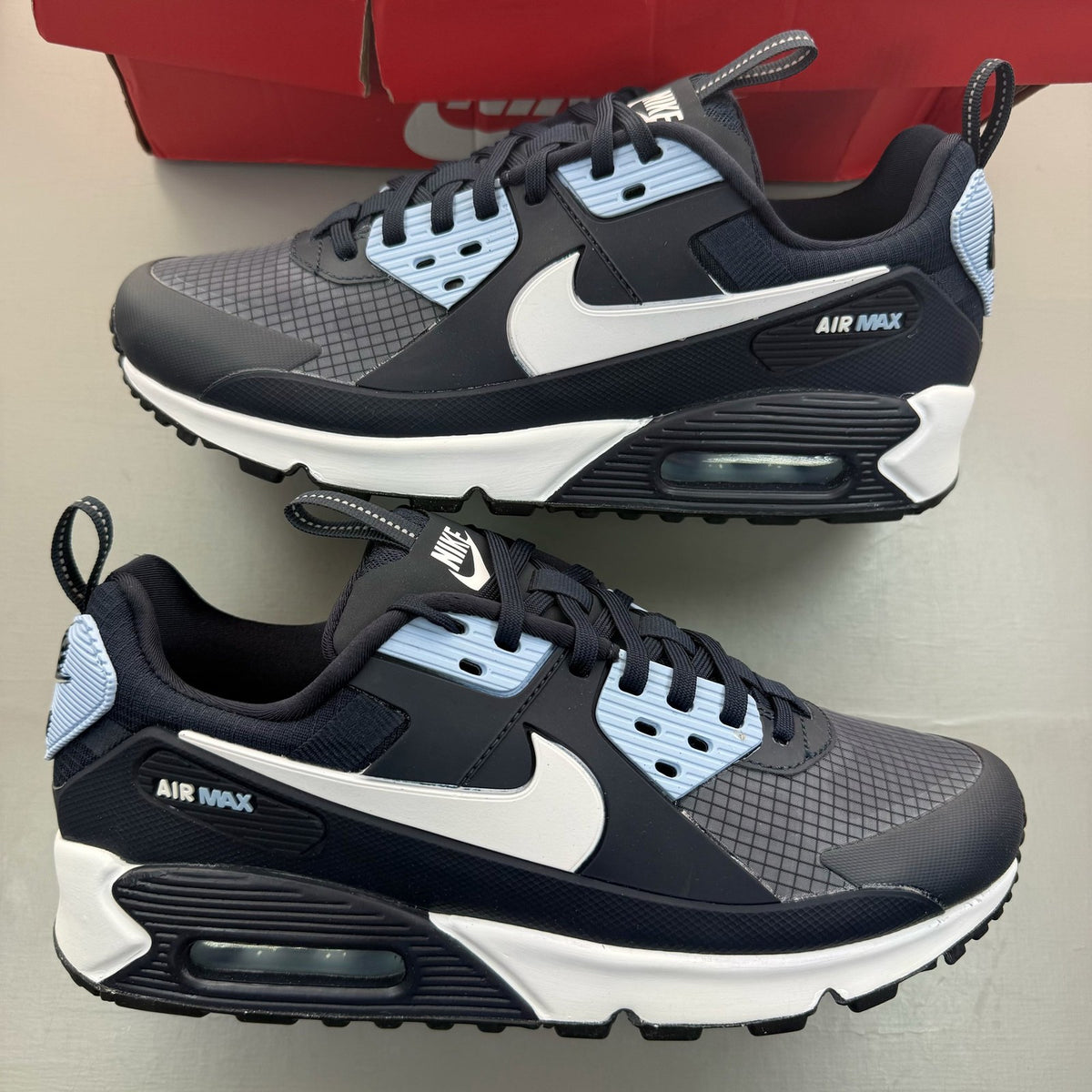 Nike Air Max 90 blue trainers with white accents and logo detail.