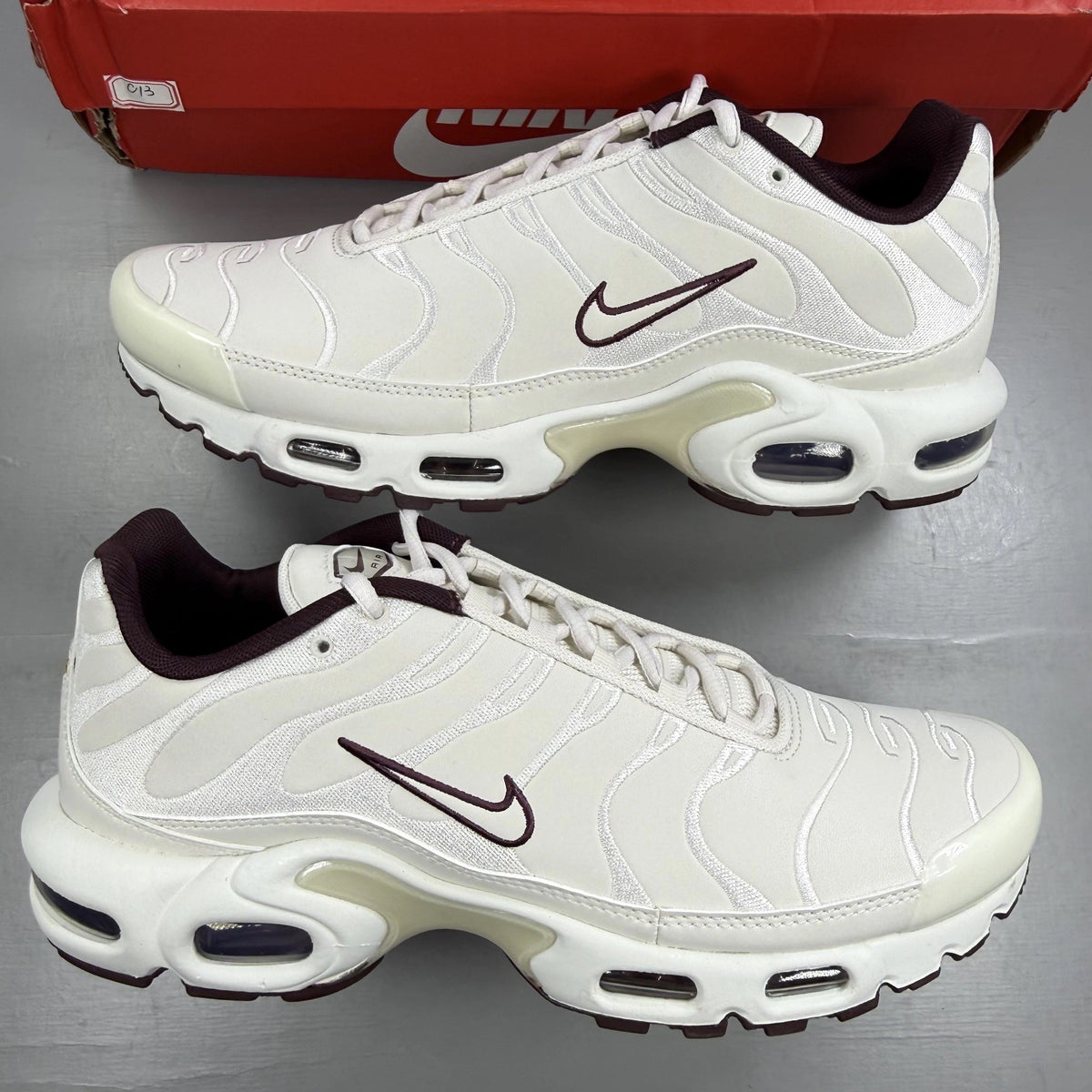 Nike Air Max Plus trainers white with burgundy accents and signature logo details.