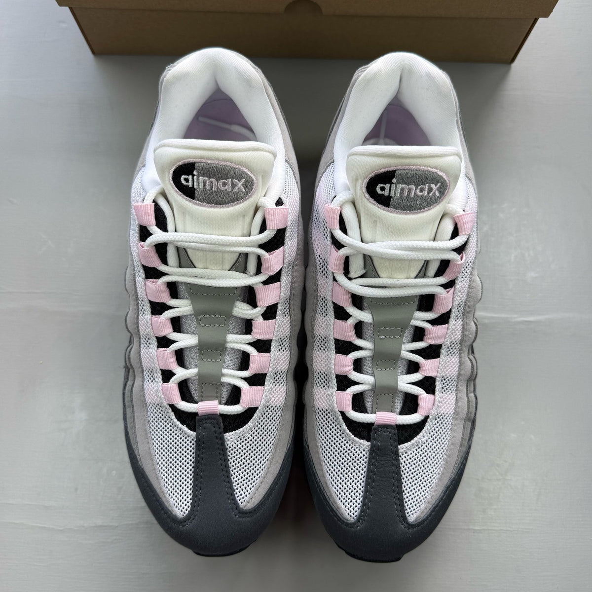 Nike Air Max 95 grey trainers with pink foam accents and black detailing.