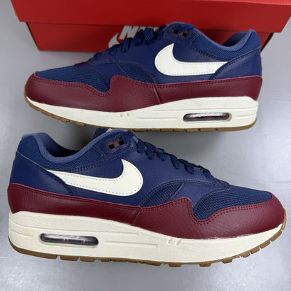 Nike Air Max 1 red trainers with navy accents and gum sole, featuring logo details.