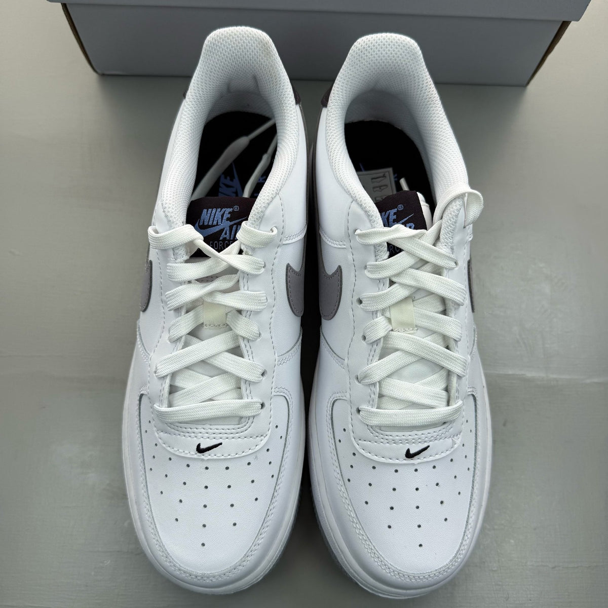 Nike Air Force 1 low white trainers with grey cement accents and logo detailing.