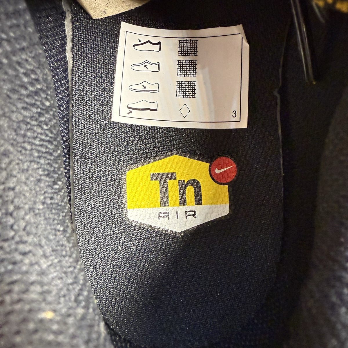 Nike Air Max Plus TN trainers black with gold accents and distinctive wavy pattern.