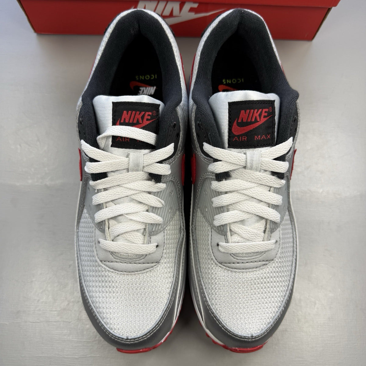 Nike Air Max 90 Icons grey trainers with red accents and white sole, featuring logo details.