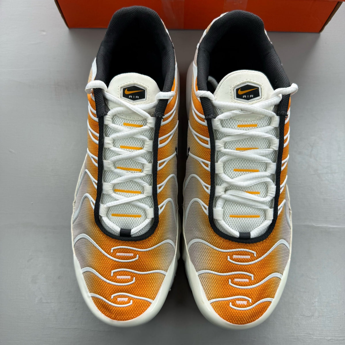 Nike Air Max Plus TN white trainers with orange accents and grey detailing.