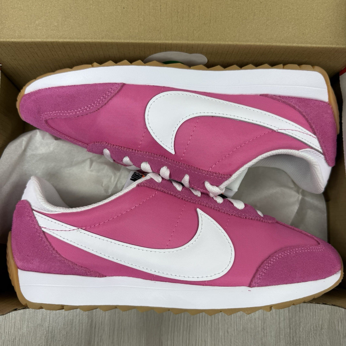 Nike white trainers with pink accents and gum sole, featuring iconic swoosh logo.