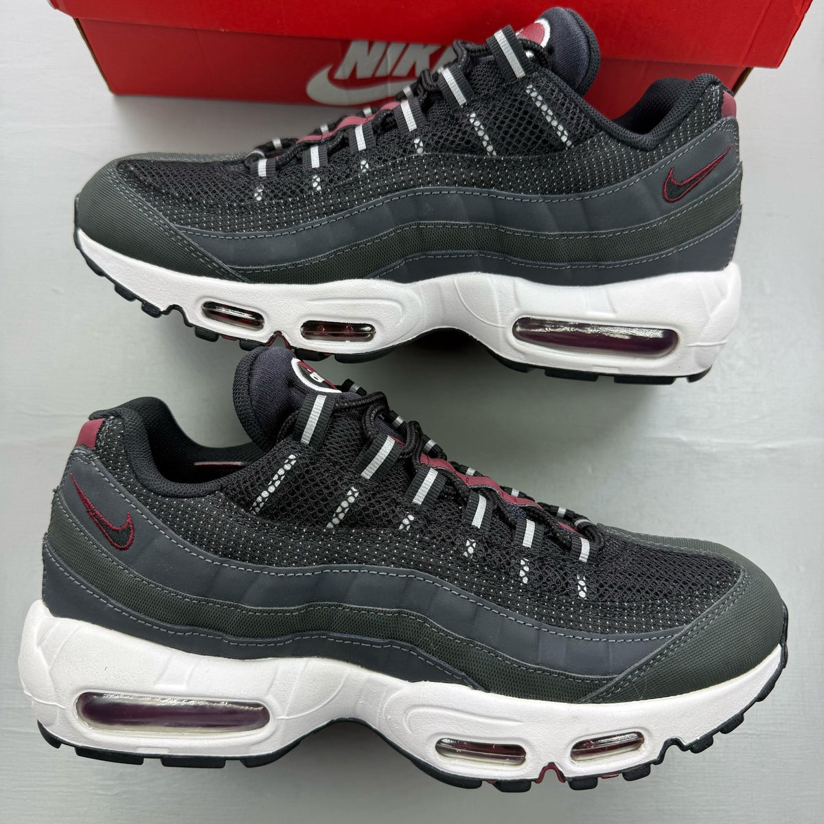 Nike black trainers with red accents and grey detailing, featuring iconic Air Max design.