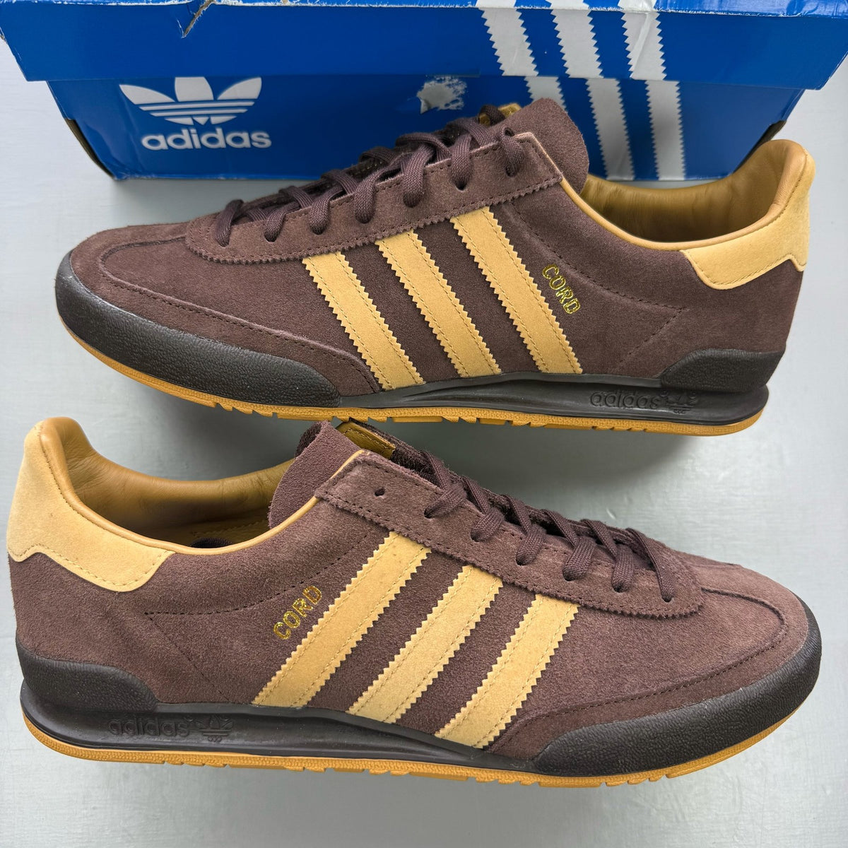 Adidas brown trainers with gold accents and gum sole, featuring iconic three stripes logo.