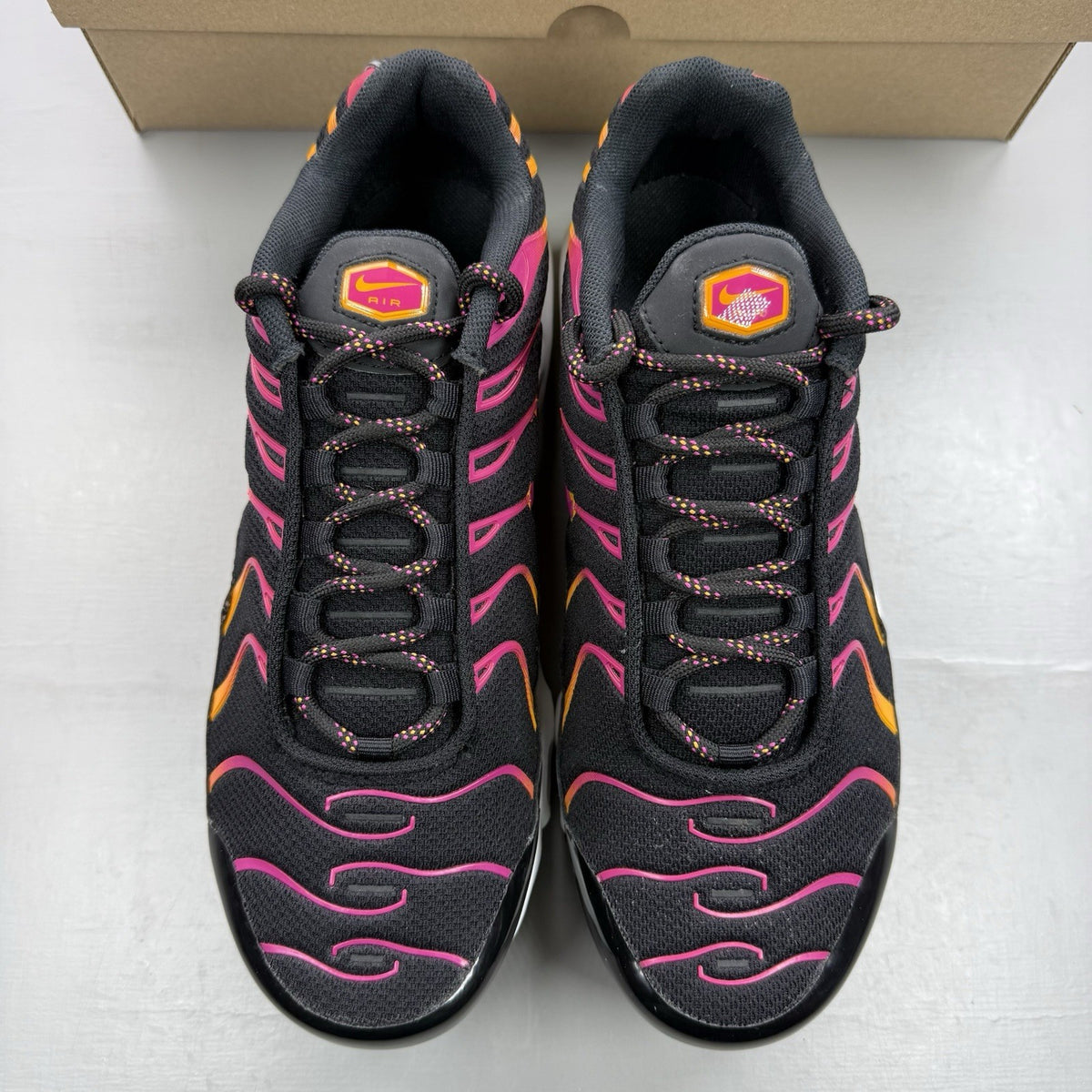 Nike Air Max Plus TN black trainers with active pink and white accents, logo detailing.