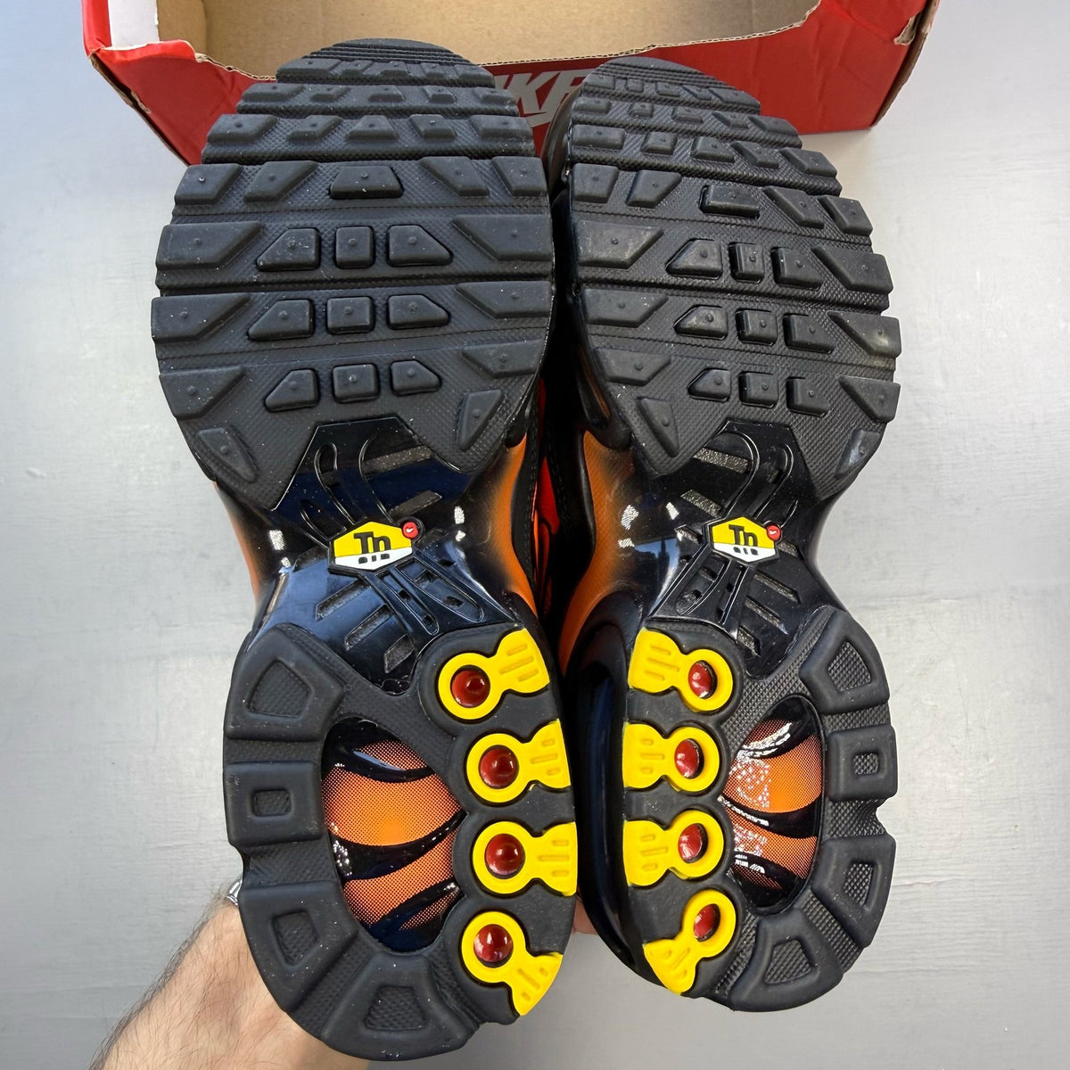 Nike Air Max Plus TN black trainers with orange accents and signature logo details.