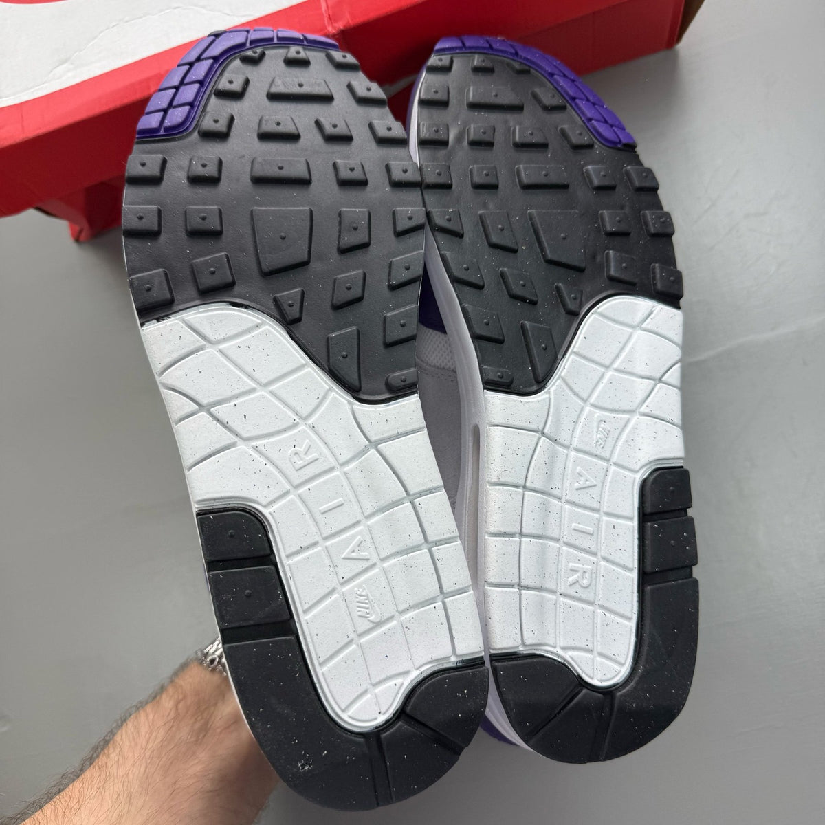Nike Air Max 1 white trainers with purple accents and logo detail.