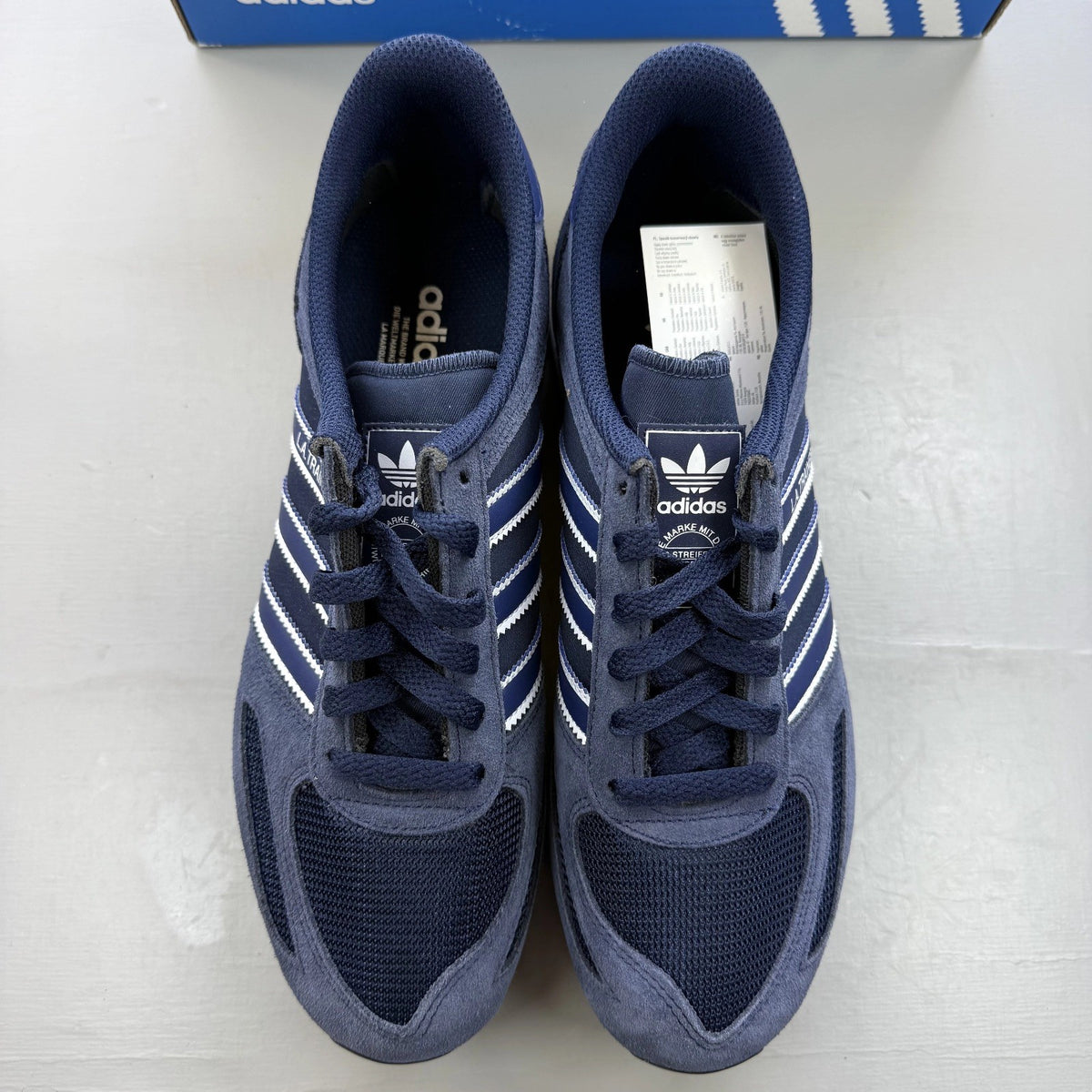 Adidas blue LA Trainer sneakers with white stripes and logo detailing.