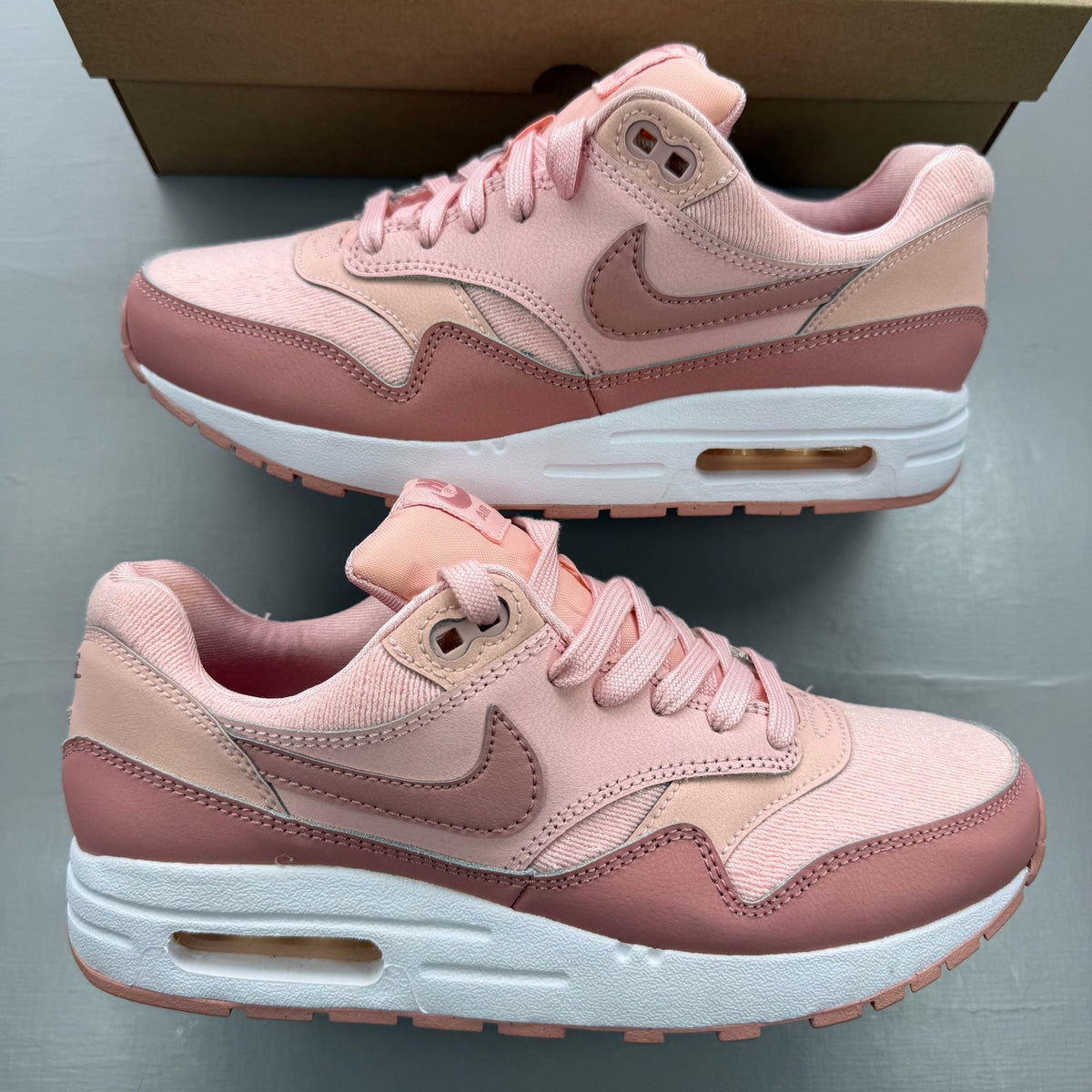 Nike Air Max 1 pink trainers with white accents and logo details.