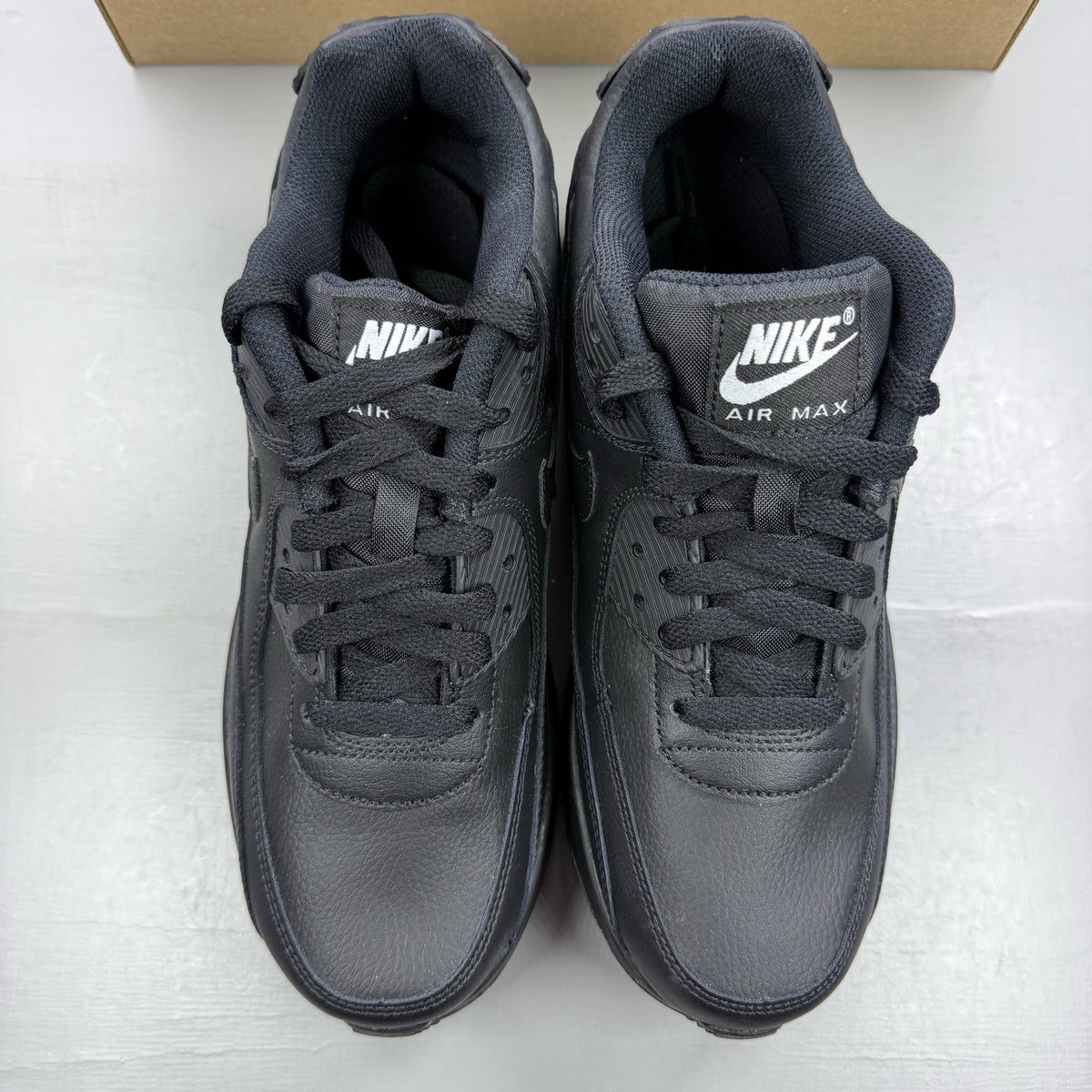 Nike Air Max 90 black leather trainers with iconic swoosh logo and textured design.