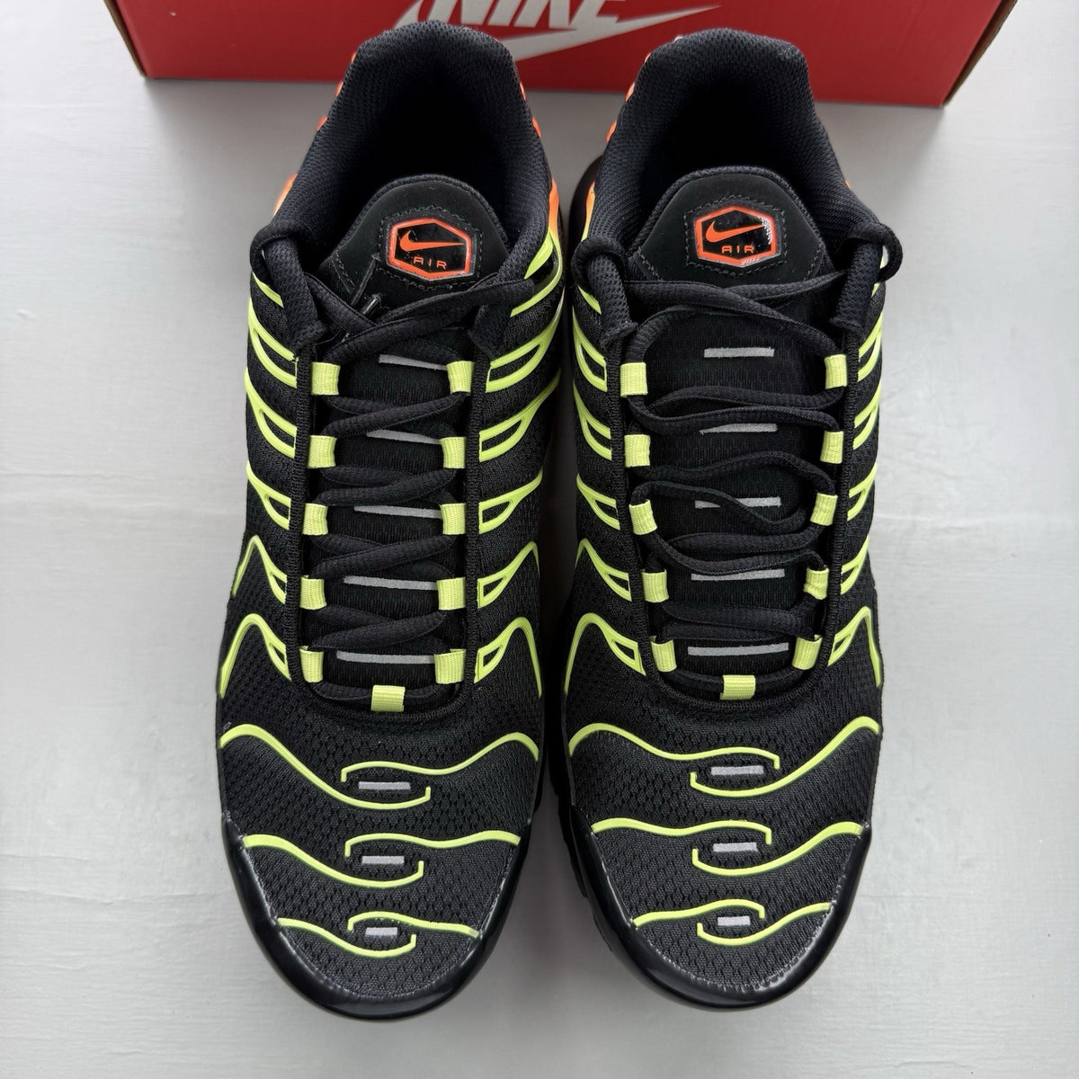 Nike Air Max Plus TN black trainers with vibrant orange and volt accents, mesh material.