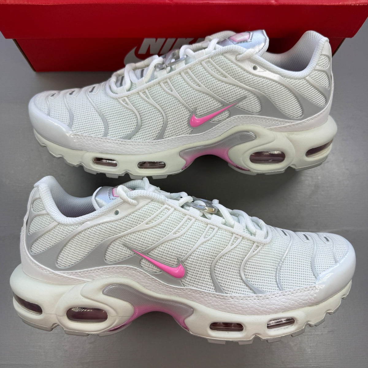 Nike athletic shoes white with pink accents and signature Air Max Plus design.