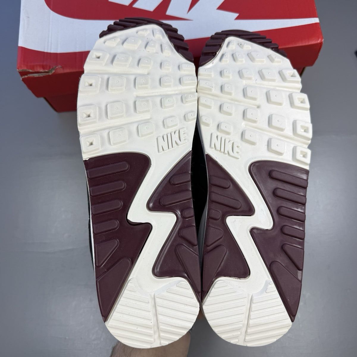 Nike Air Max 90 grey trainers with burgundy accents and black detailing.