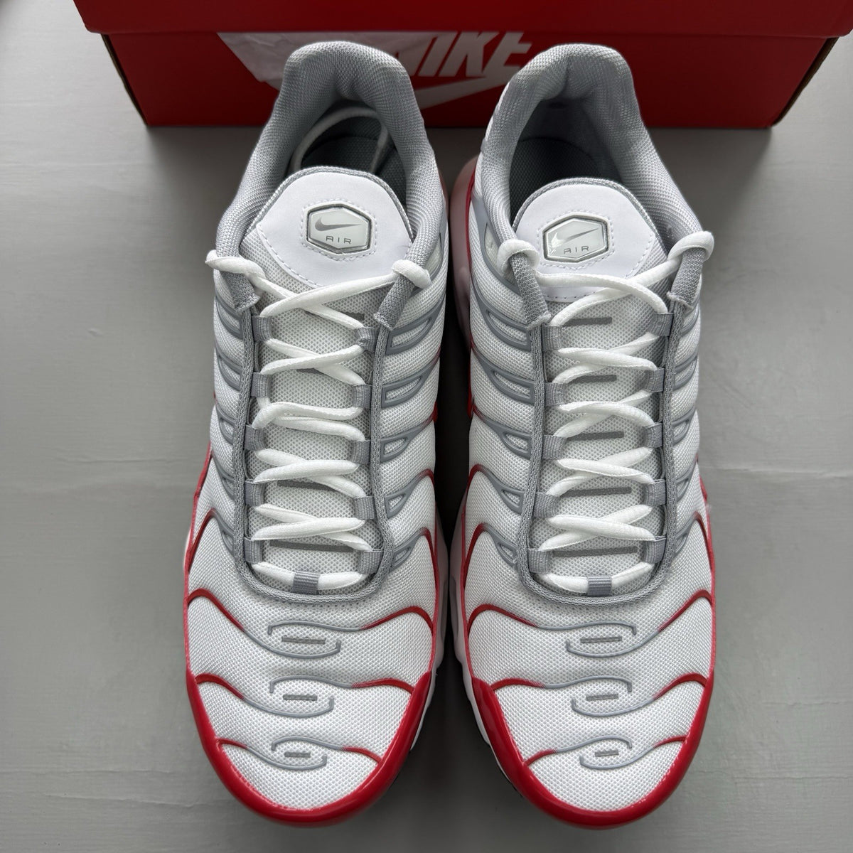 Nike Air Max Plus TN white trainers with university red and grey accents, featuring signature logo.