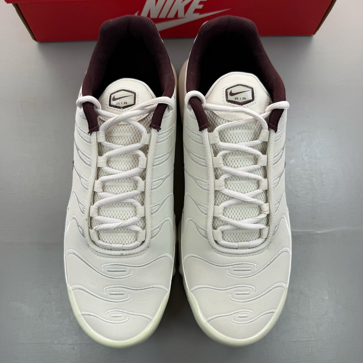 Nike Air Max Plus TN white trainers with burgundy accents and visible logo details.