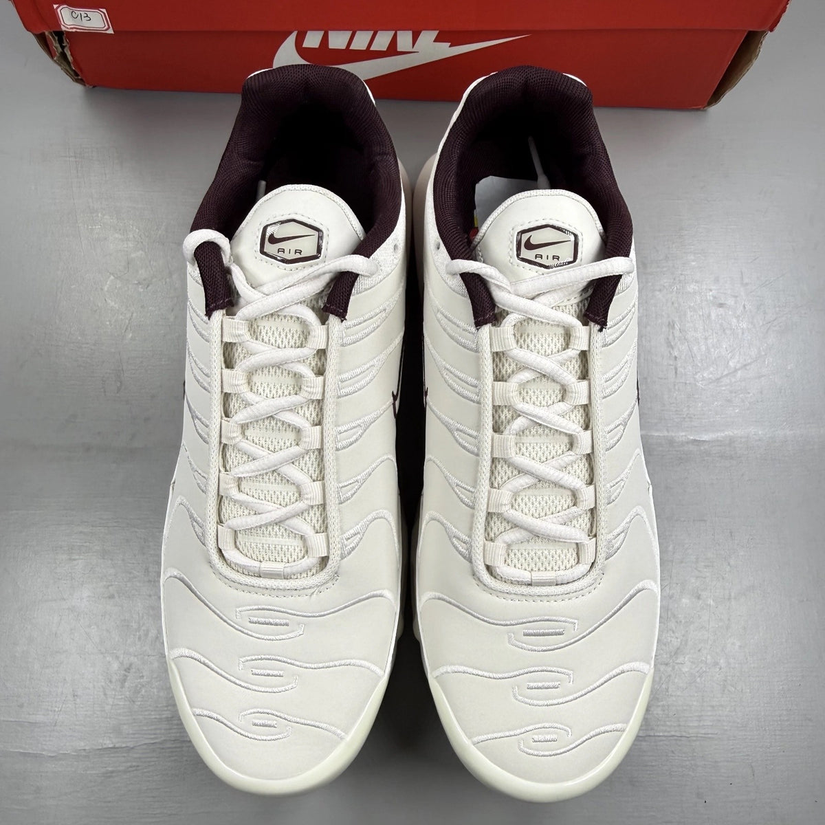 Nike Air Max Plus trainers white with burgundy accents and signature logo details.