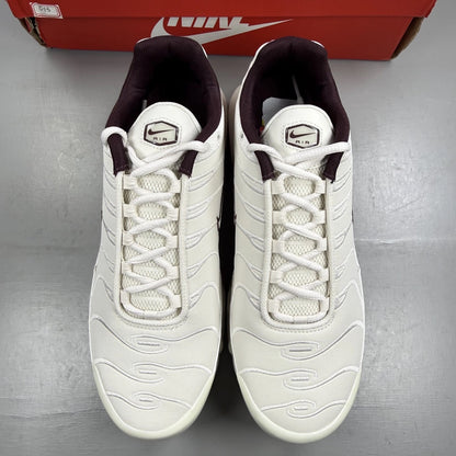 Nike Air Max Plus trainers white with burgundy accents and signature logo details.