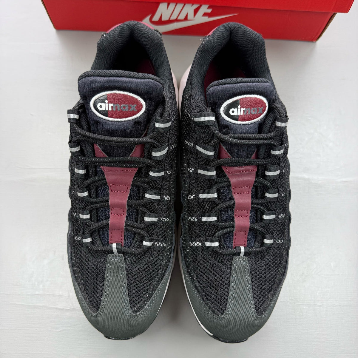 Nike black trainers with red accents and grey detailing, featuring iconic Air Max design.