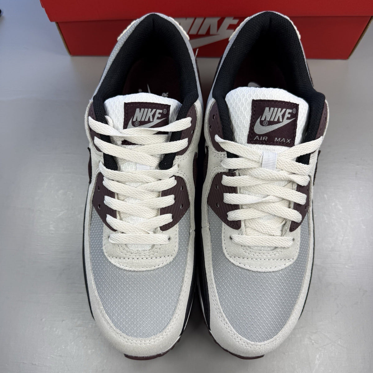 Nike Air Max 90 grey trainers with burgundy accents and black detailing.