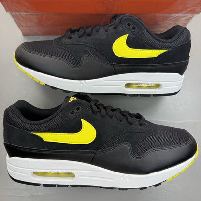 Nike Air Max 1 Essential black trainers with yellow accents and logo detail.